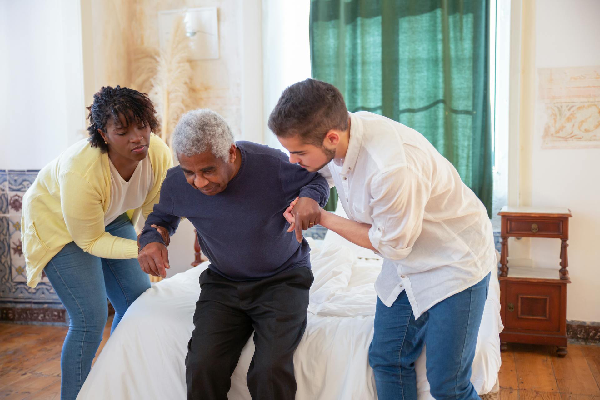two people helping a senior to sit on the bed